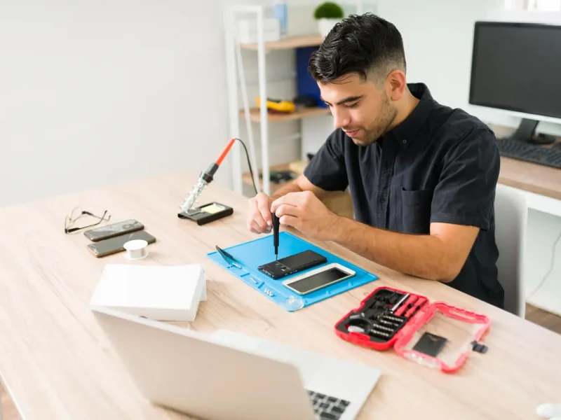 handsome-young-man-smiling-while-repairing-old-smartphone-male-technician-using-screwdriver-fix-broken-cellphone-workshop copiar